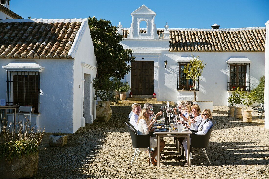 Group of adults sitting at long table in cobbled courtyard of Mediterranean country house
