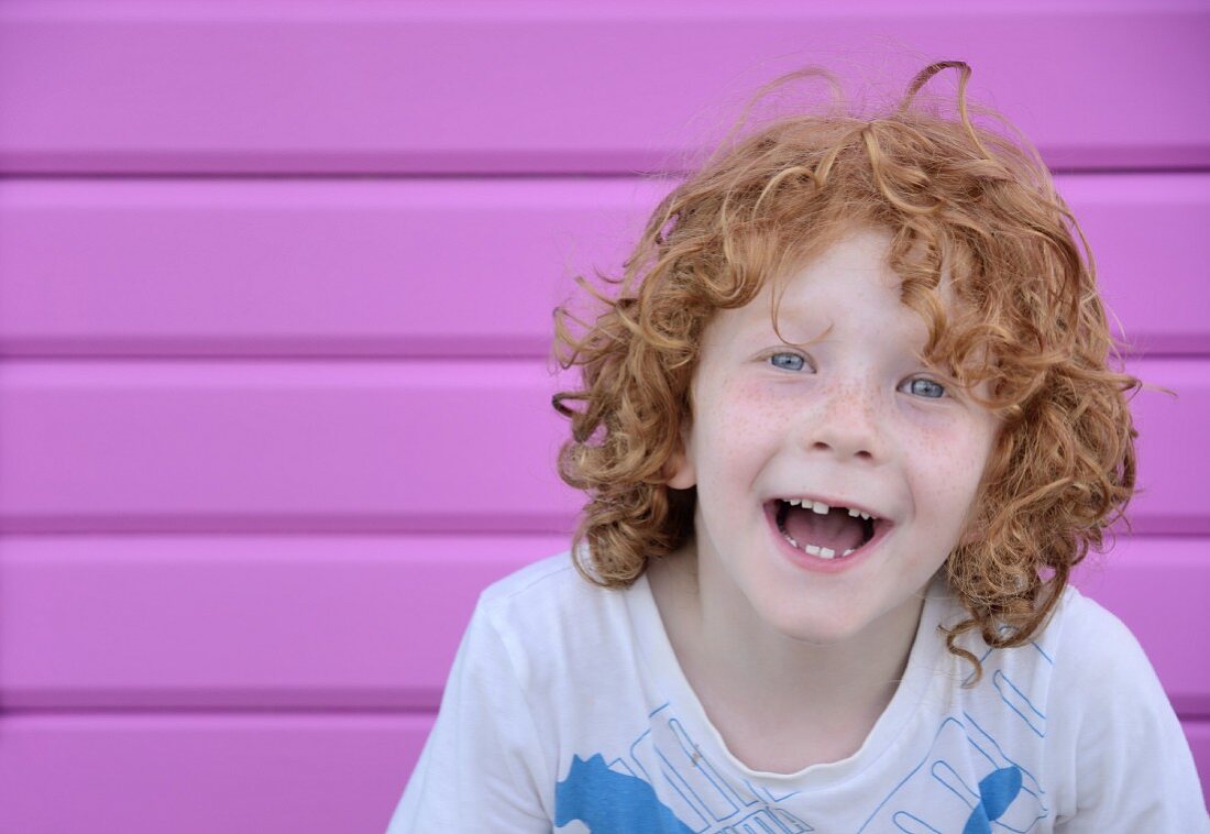 Lachendes Kind vor pinkfarbener Holzwand