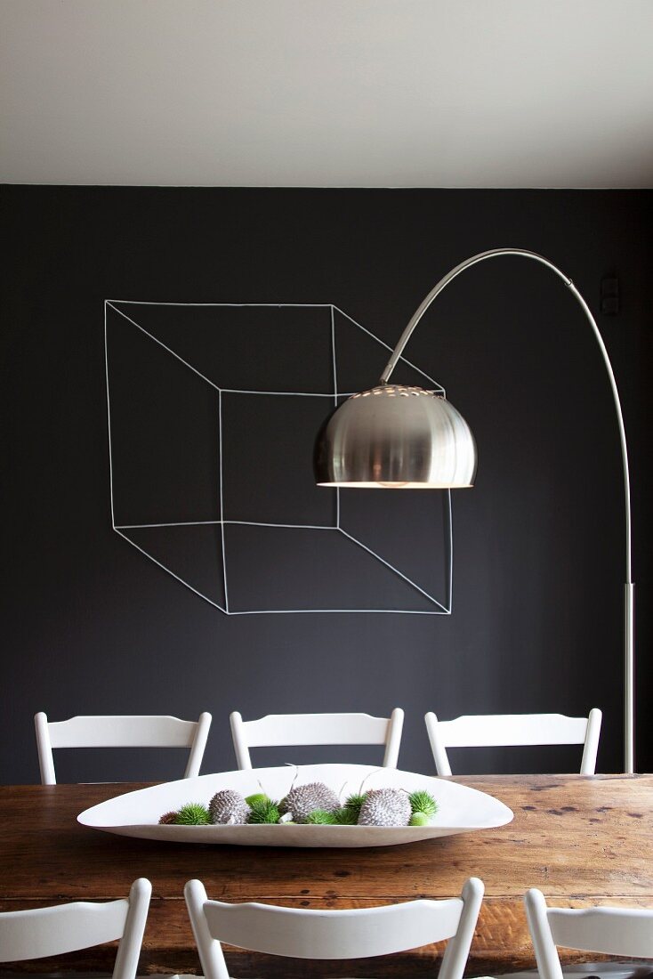 weiße Schale auf rustikalem Holztisch und Bogenlampe vor schwarz getönter Wand mit Würfel-Zeichung