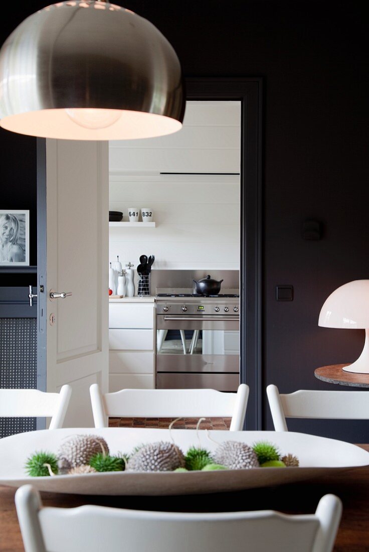 Designer-Hängeleuchte mit Metallschirm über Esstisch vor offener Tür und Blick in die Küche
