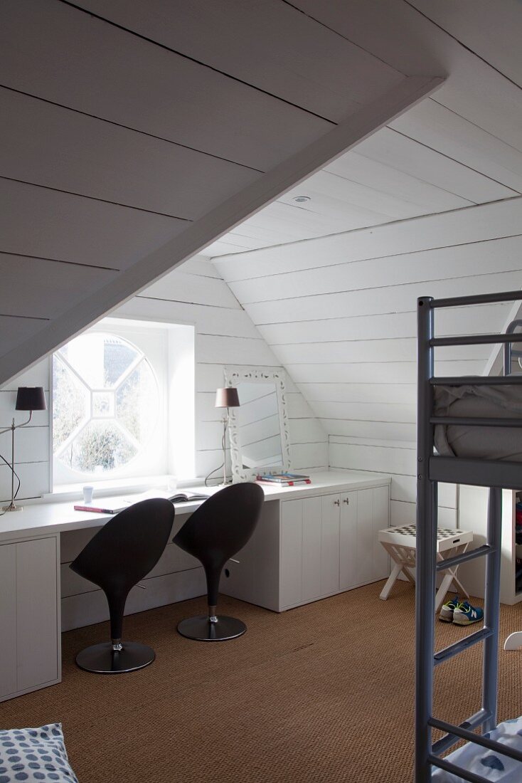 Arbeitstisch mit schwarzen Designer-Drehstühlen am Fenster im Dachzimmer