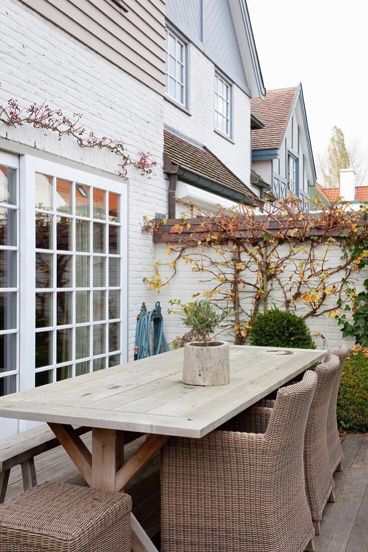 Rattanstühle und rustikaler Holztisch auf Terrasse vor Terrassentür mit Sprossenfenstern