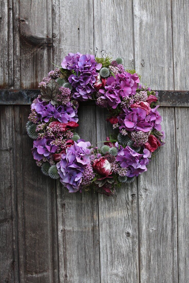 Purple wreath with thistles, radicchio leaves, hydrangea and marjoram flowers on wooden door