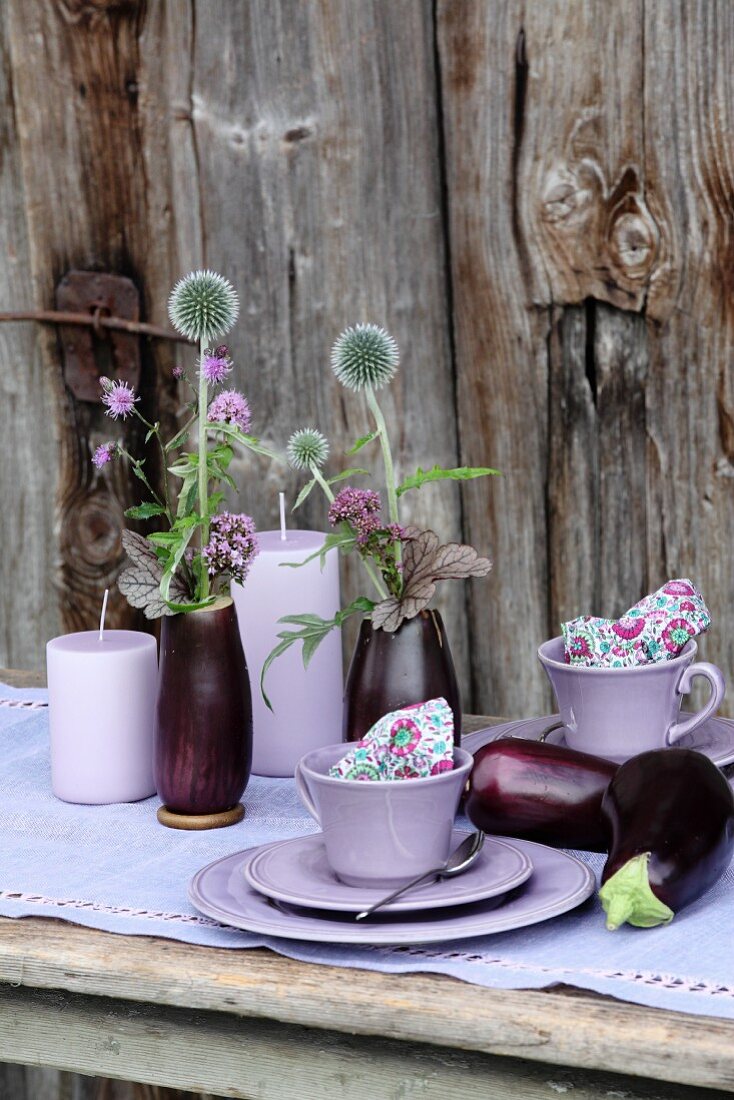 Posies of thistles and marjoram flowers in hollowed-out aubergines decorating table