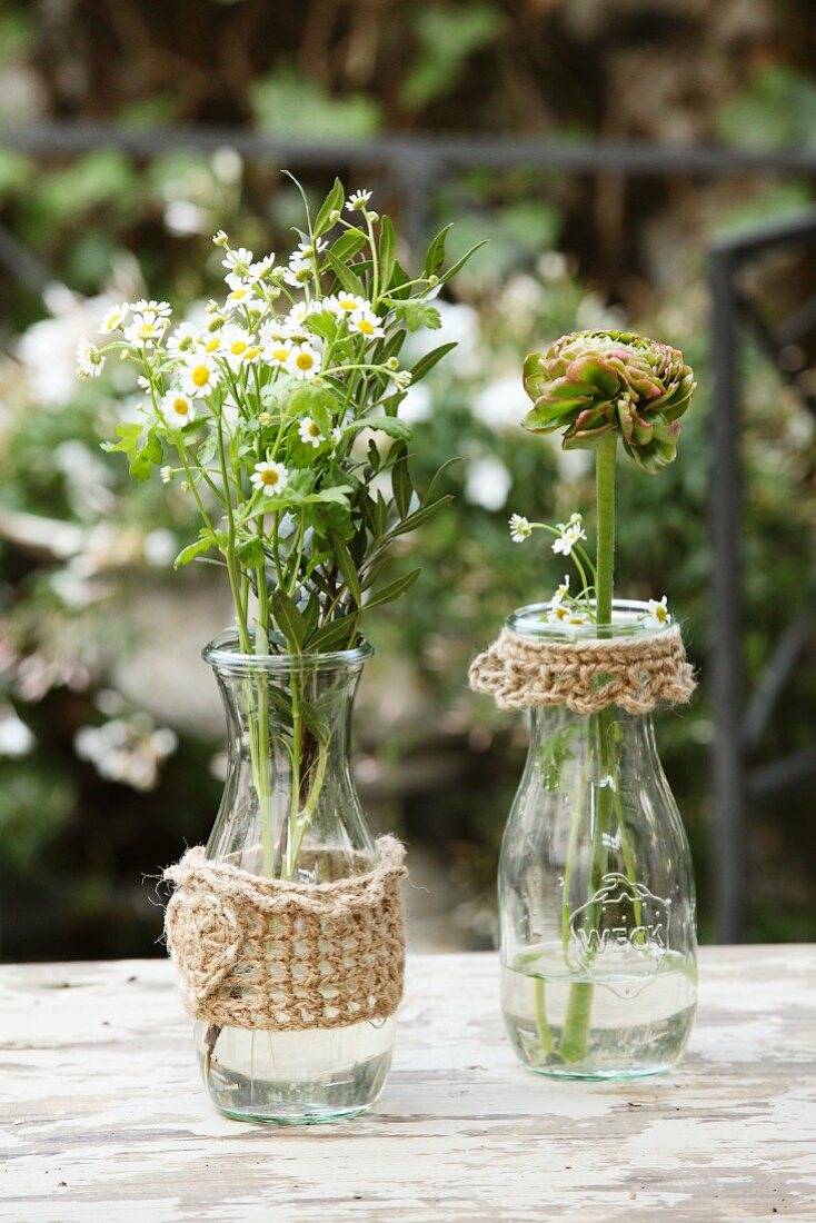 Glass bottles with hand-knitted covers and trims on table in garden