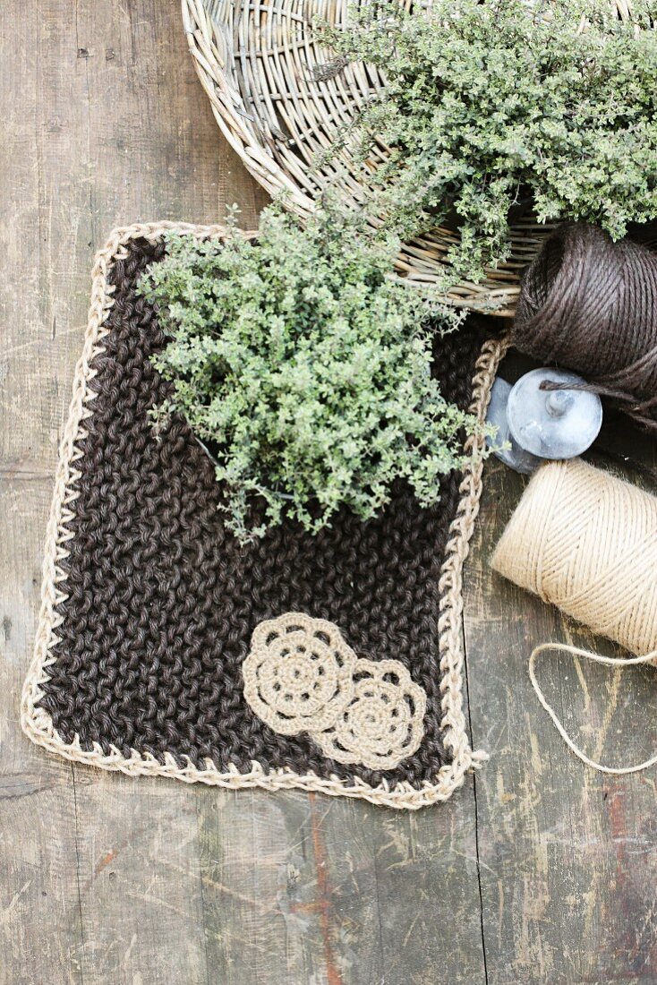 Hand-made pot holder next to reels of yarn & posies of herbs in wicker dish