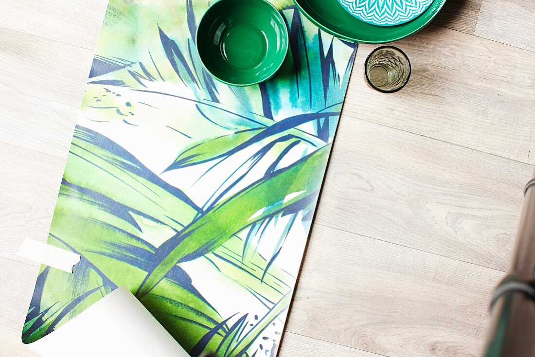 Green ceramic bowls arranged on length of jungle-patterned wallpaper on wooden floor