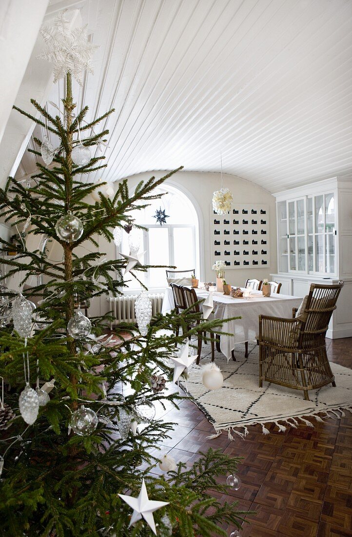 Christmas tree decorated with white stars and glass baubles; dining room with wood-clad, white-painted barrel vaulted ceiling and mosaic parquet floor