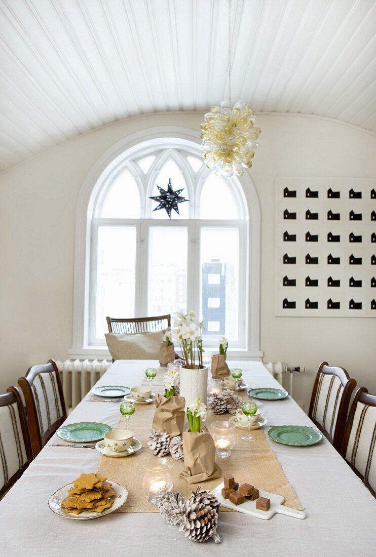 In zarten Farben weihnachtlich gedeckter Tisch; Esszimmer mit Glasballonlüster an gewölbter Holzdecke und Rundbogenfenster