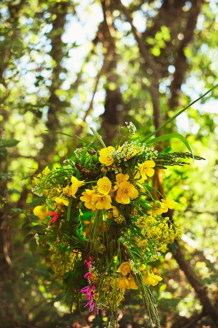 Sommerlicher Blumenkranz in überwiegenden Gelbtönen vor einer verschwommenen Baumkulissentapete
