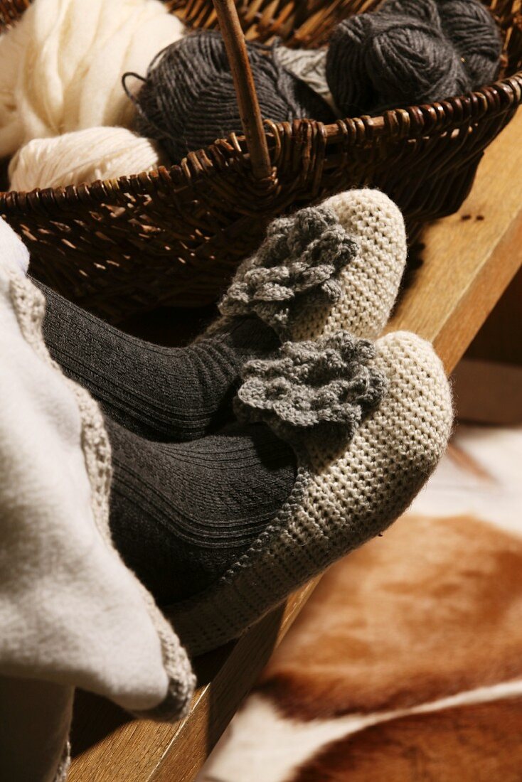 Hand-crocheted slippers on woman's feet next to basket of wool
