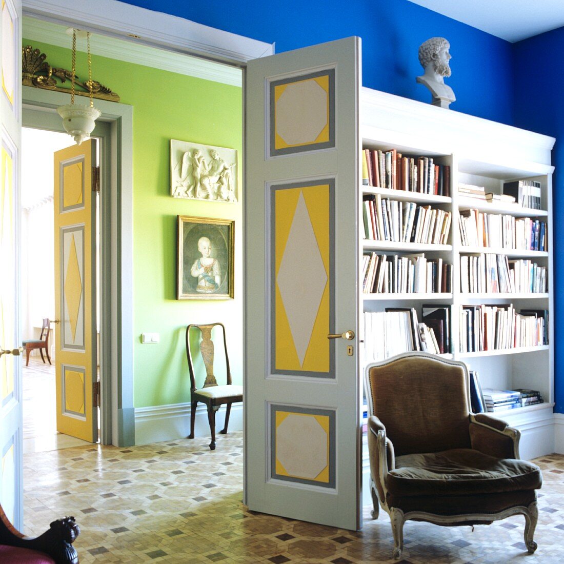 Rokoko Sessel vor Einbauregal mit Büchern in blauem Zimmer; Blick durch offene Flügeltür in grünes Zimmer in herrschaftlichem Haus