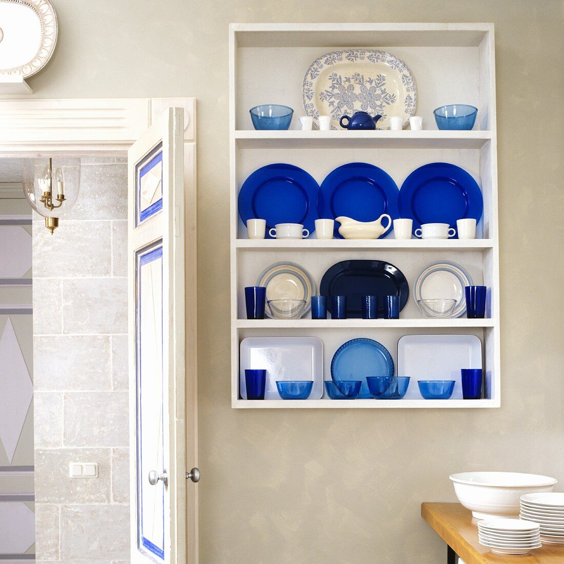Blue and white crockery in wall-mounted shelves next to open door