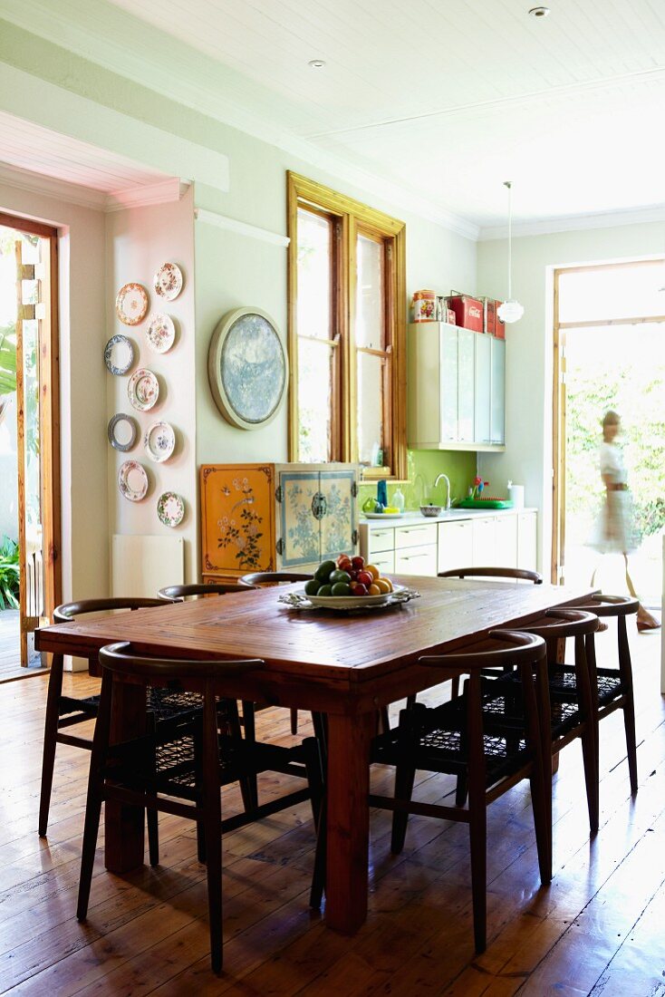 Dark wooden chairs around table on rustic board floor in kitchen-dining room with walls in pastel shades