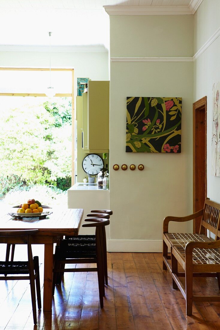 Dunkle Holzstühle um Tisch und Sitzbank an Wand in Wohnküche mit offener Terrassentür