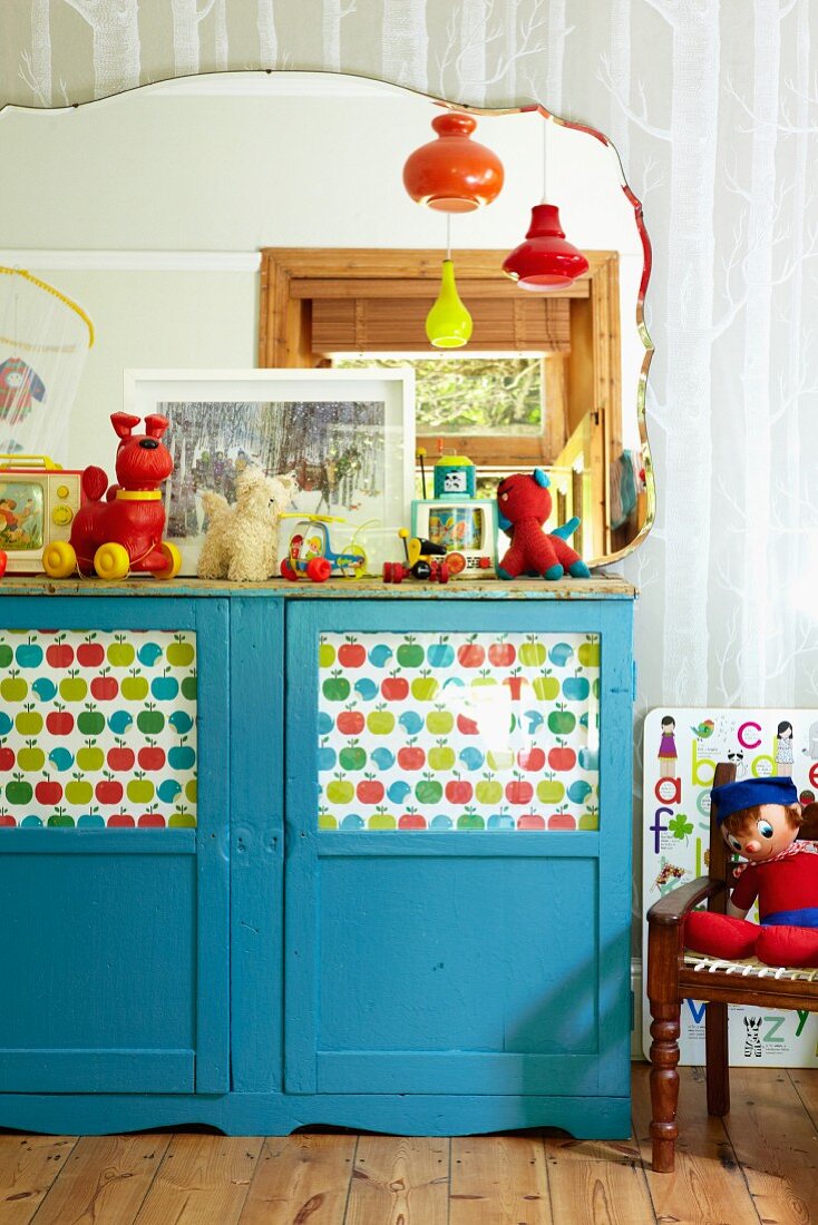 Blue-painted, half-height cabinet with printed paper behind glass door panels in child's bedroom