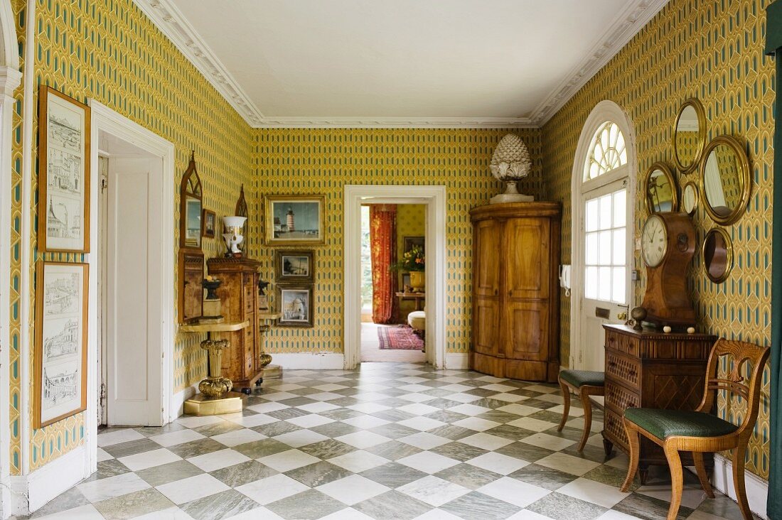 Spacious foyer with antique, 18th century furniture, boldly patterned wallpaper and diagonal, chequered marble floor tiles