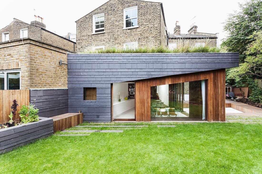 Modern extension with slate and wood cladding; traditional brick house in background