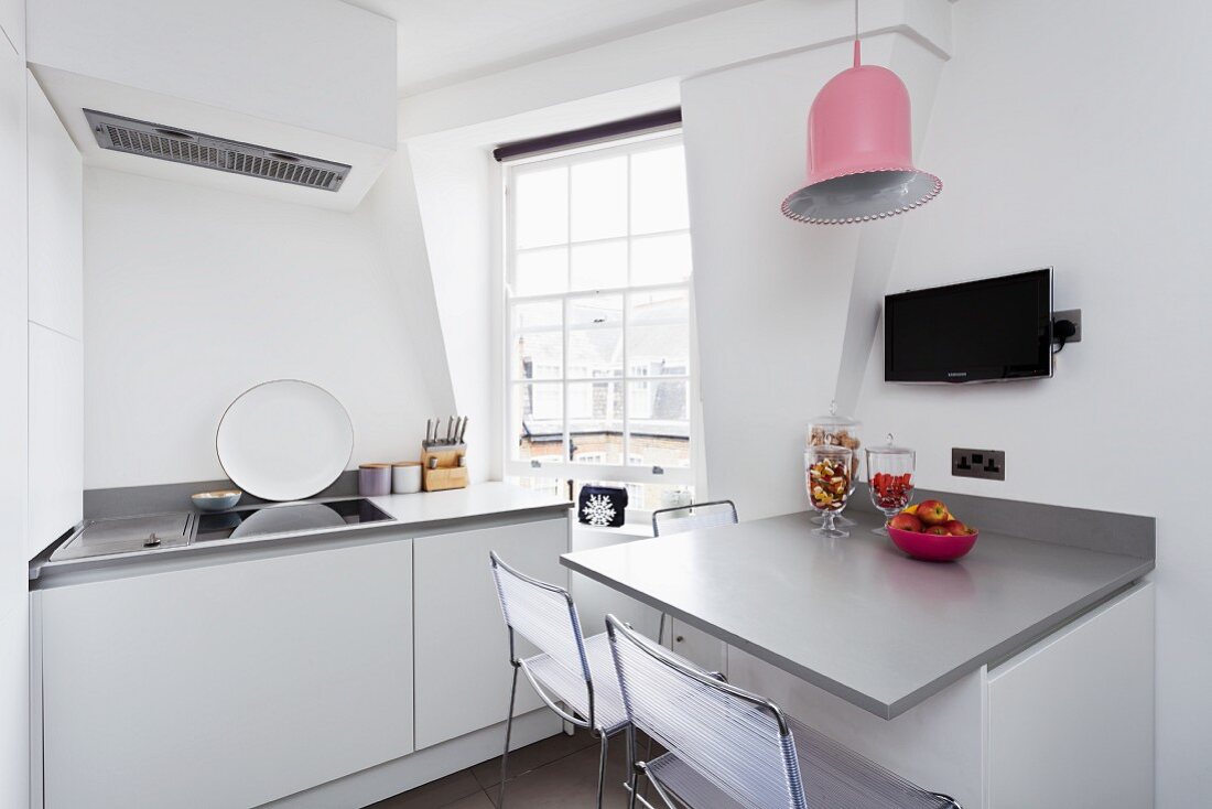 Moderne, weiße Küche mit grauem Wandtisch und einer glockenförmigen Hängelampe in Pink