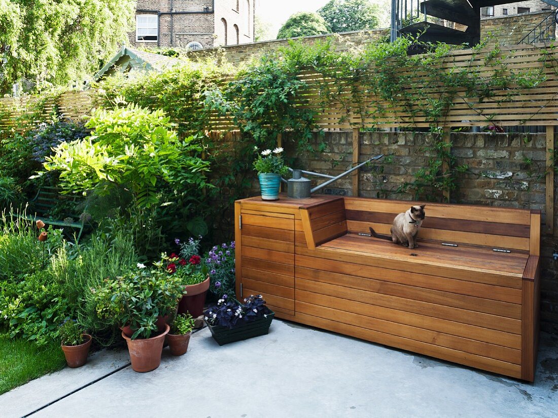 Terrace with concrete floor and wooden bench structure with storage for garden tools and utensils against old brick wall