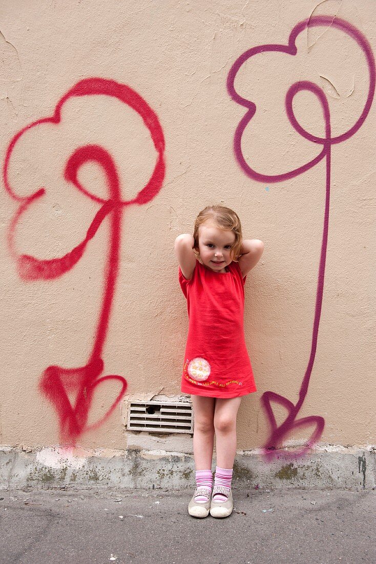 Kleines Mädchen steht vor einer mit Blumen besprühten Wand