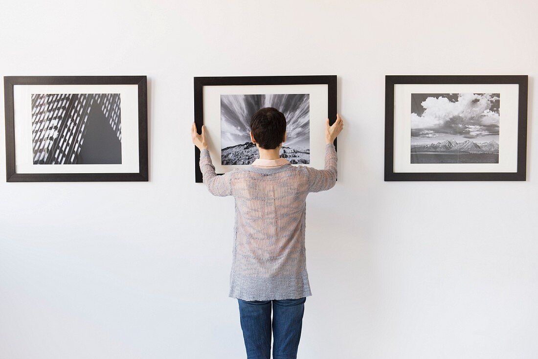 Frau hängt Fotos in einer Galerie auf