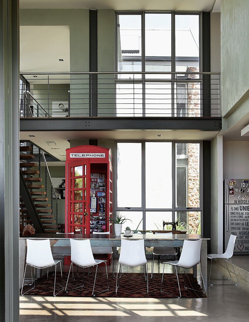 Open-plan interior with dining table, English telephone box as decoration & staircase leading to gallery