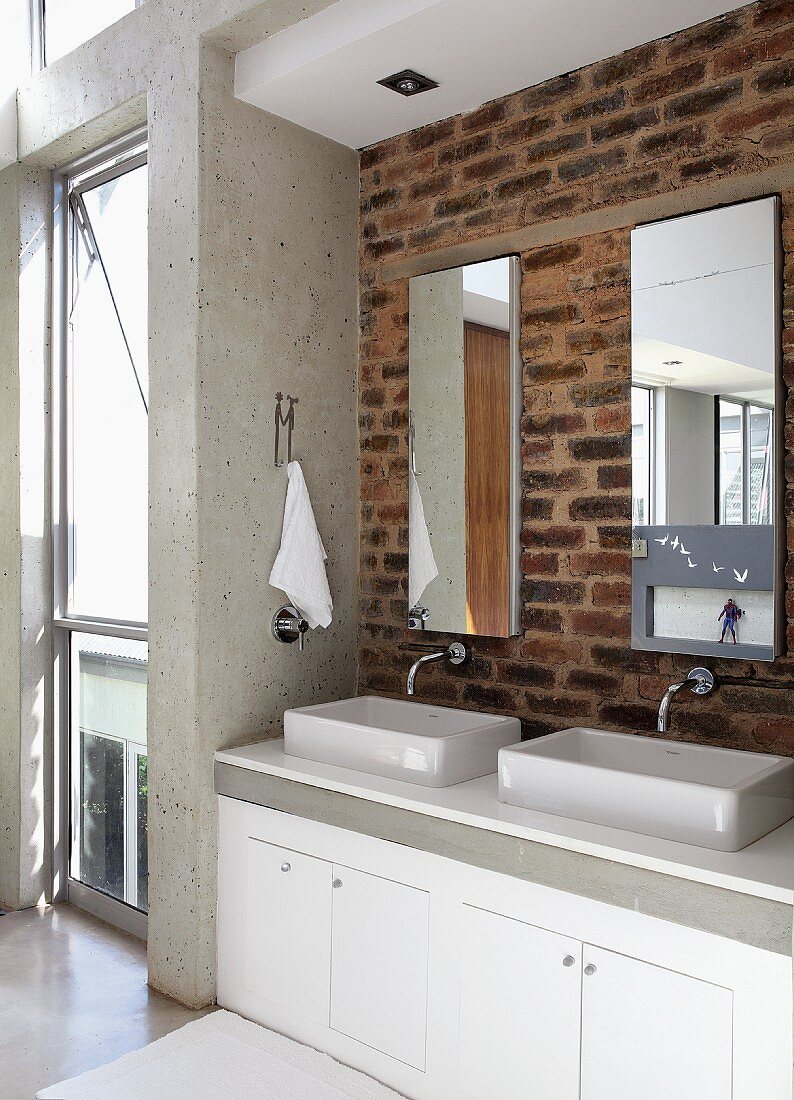 Twin basins on washstand below mirrors on brick wall