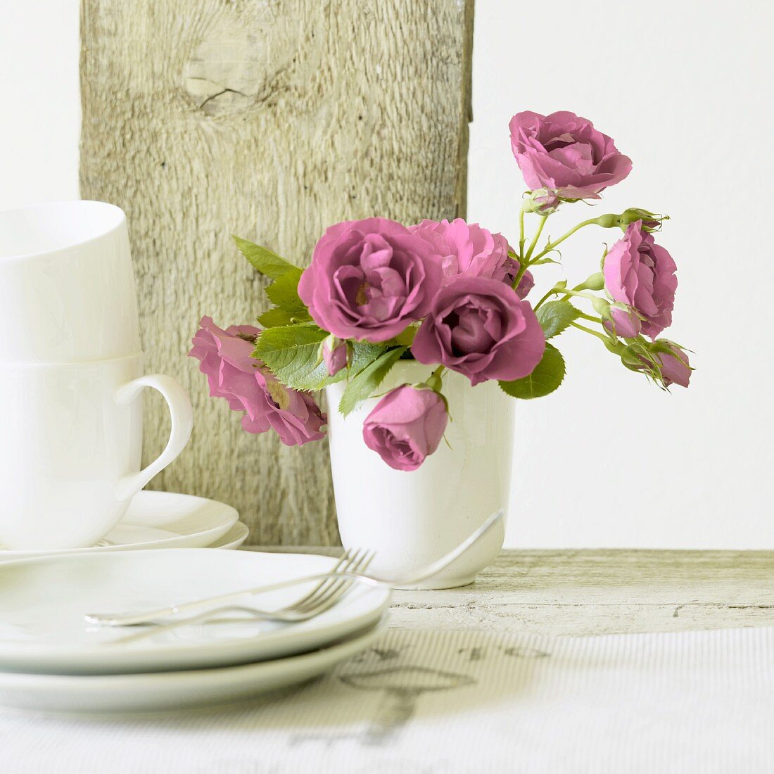 Pinkfarbene Rosen in einer Keramikvase, Kaffeetassen und Kuchenteller