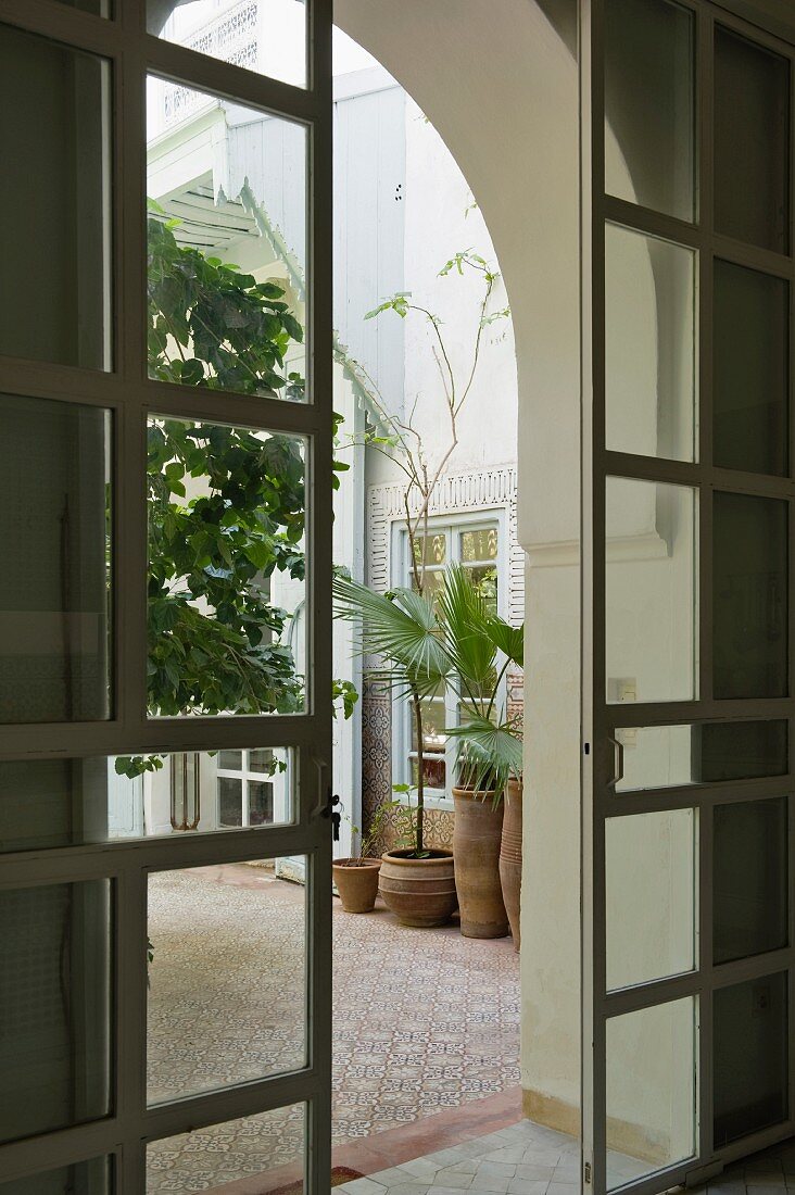 Blick durch geöffnete Schiebetüren in marokkanischen Innenhof mit Topfpflanzen auf Mosaikfliesen