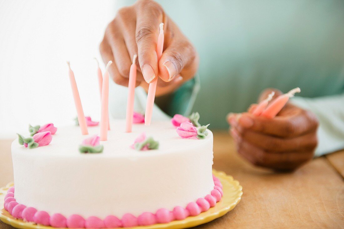 Hand steckt Kerzen auf Geburtstagstorte
