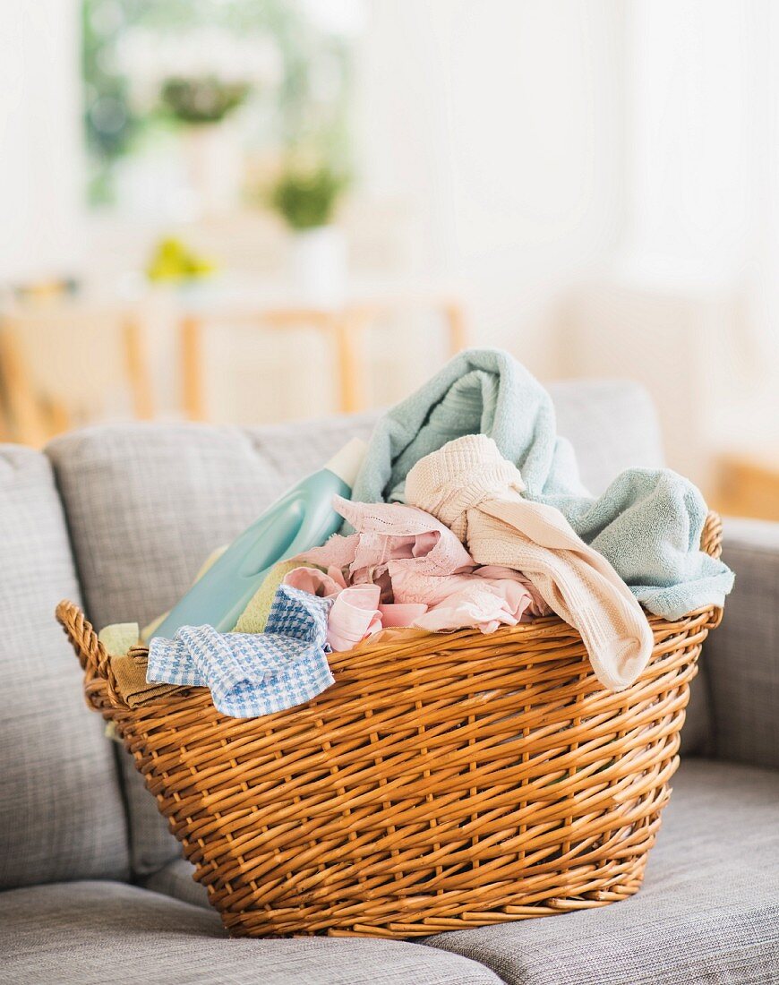 Dirty laundry & bottle of laundry detergent in basket on sofa