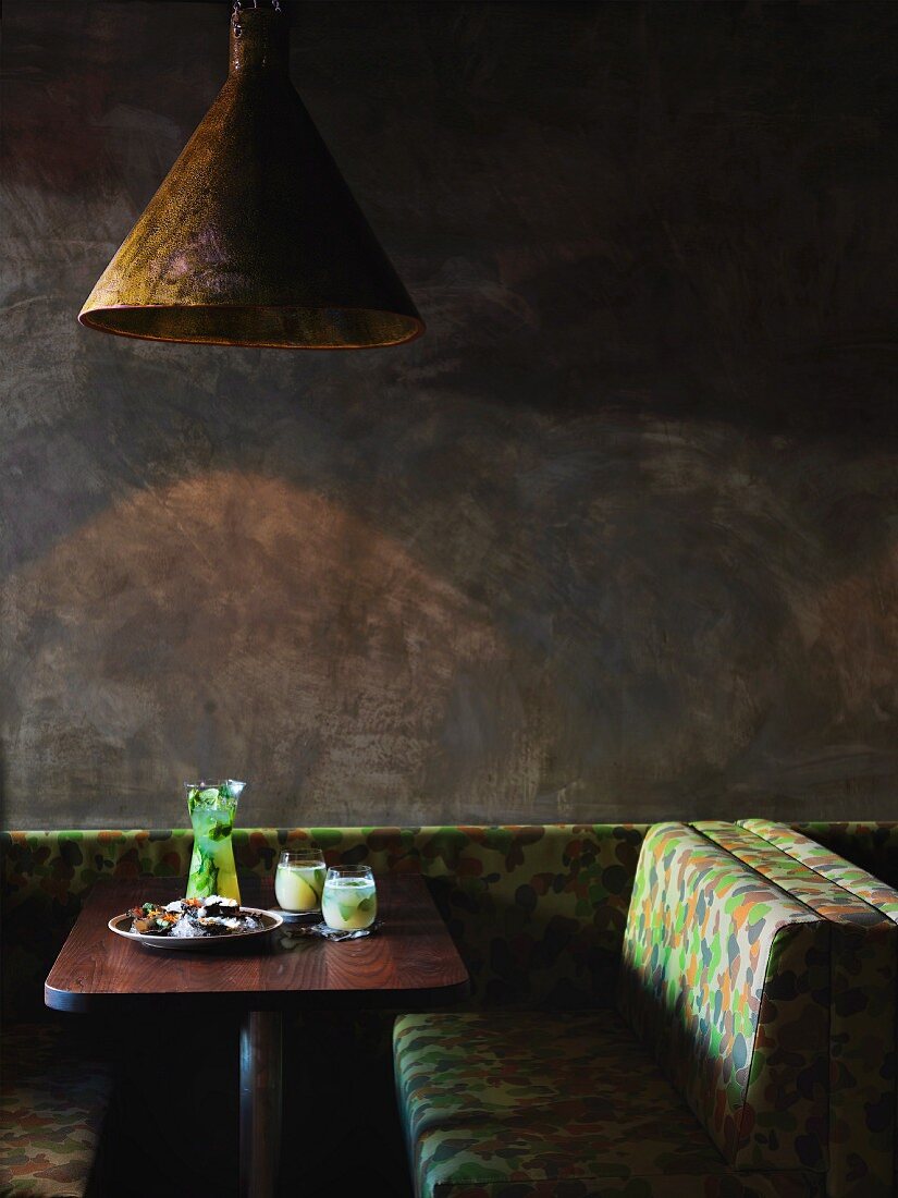 Restaurant table against grey wall with freshly served platter of oysters and cocktails; rustic pendant lamp above table