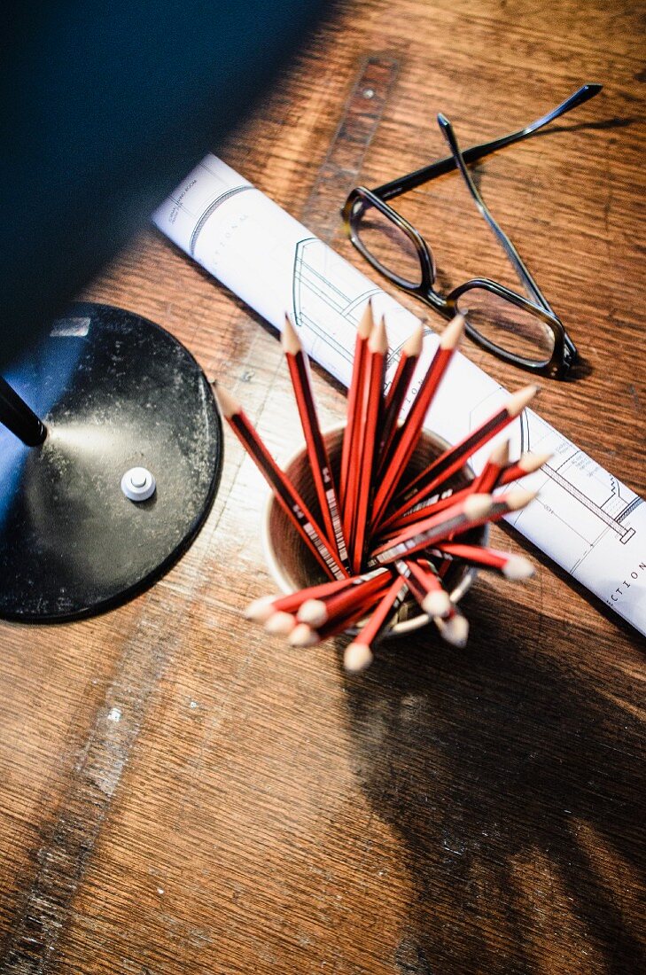 View down onto pot of pencils and spectacles on wooden surface