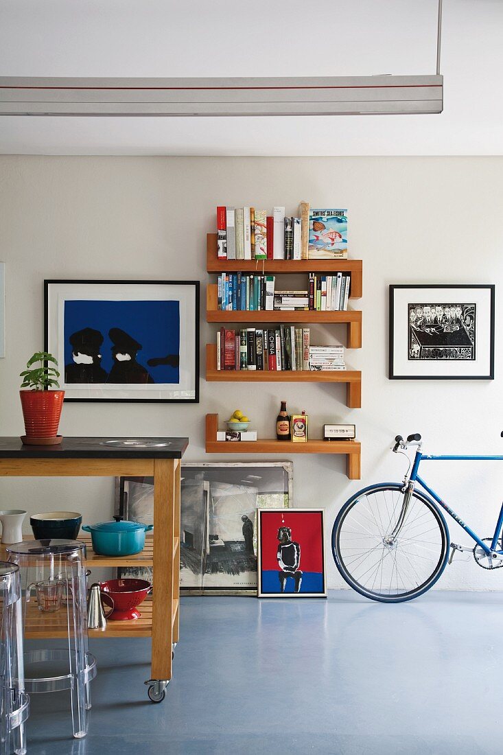 Kücheninsel auf Rollen mit Designer Hockern aus Plexiglas (Ghost); an der Wand im Hintergrund verschiedene Bilder, Bücherboarde und ein Rennrad
