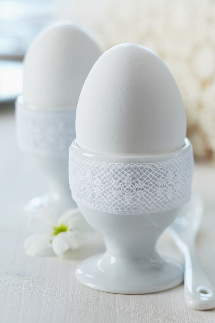 Eggcups trimmed with white lace ribbon as romantic decorations on breakfast table
