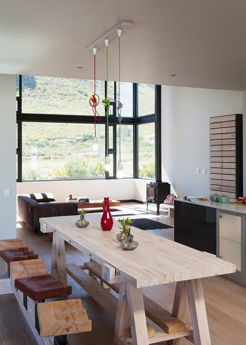 Holz-Esstisch im Werkbankstil mit Hockern in offenem Wohnraum; Loungebereich im Erker mit Panoramafenster