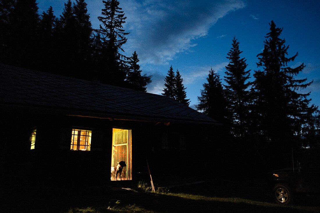 Alpine cabin at dusk with light pouring through open door