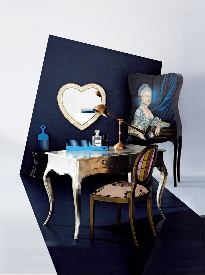 Barocker Schminktisch mit modernem Kunststoffkamm vor gestalteter dunkelblauer Wand mit Herzspiegel und barockem Frauenportrait; Bodenbelag geht in Wand über