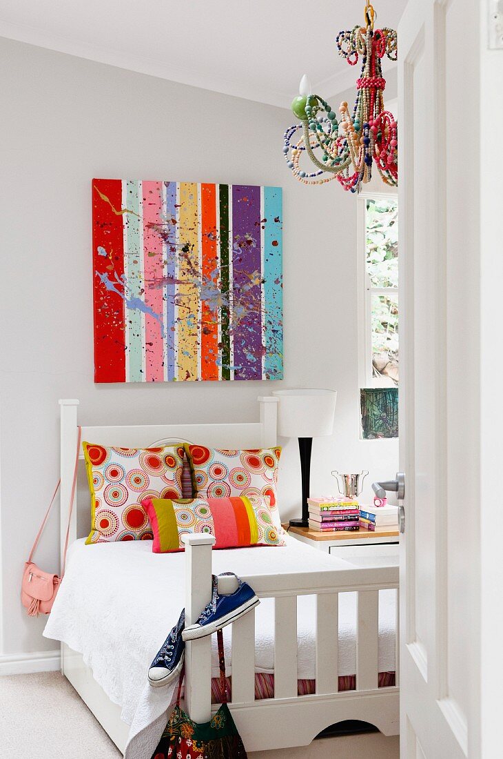 Colourful artwork above white bed in girl's bedroom