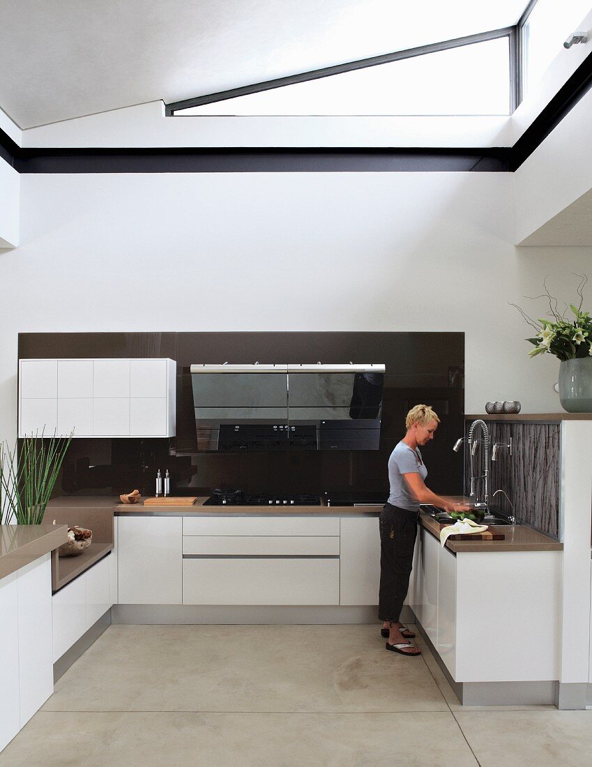 Offene Designer Einbauküche in Weiß mit dreieckigem Oberlicht in Wand; Frau vor Küchenzeile