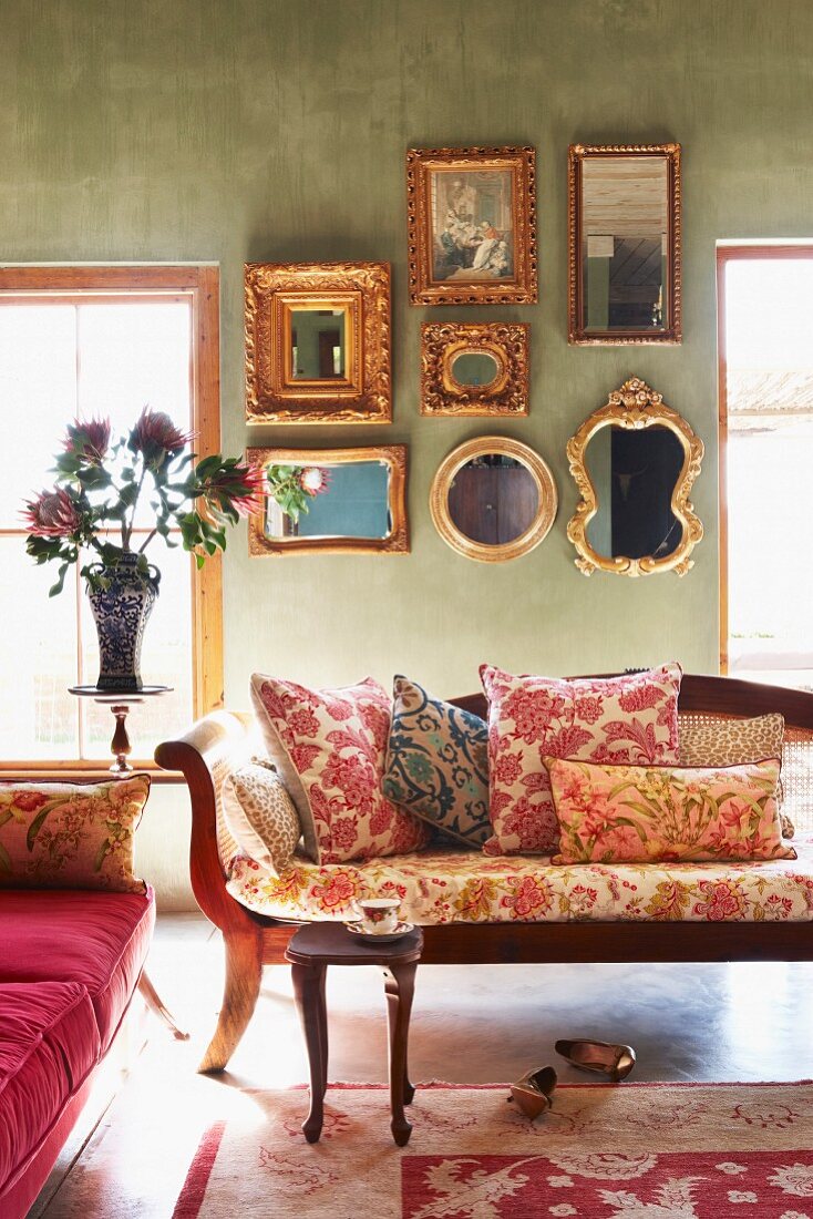 Kissen mit verschiedenen Mustern auf antiker Sitzbank in salonähnlichem Raum mit gerahmter Spiegelsammlung an grüner Wand