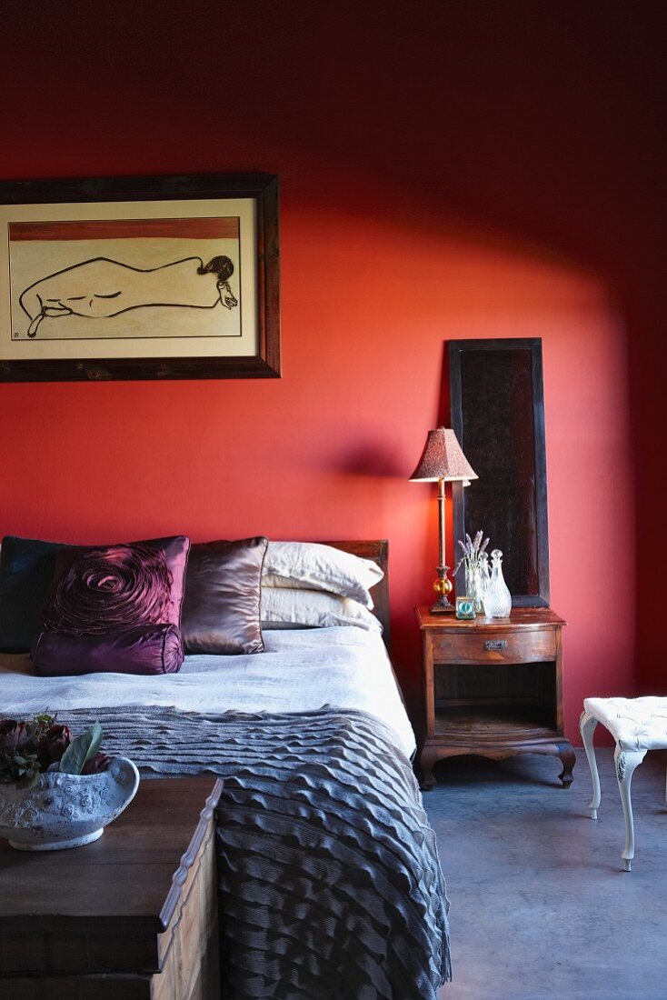 Kissen mit Satinbezug auf Bett vor rotgetönter Wand in modernem Schlafzimmer