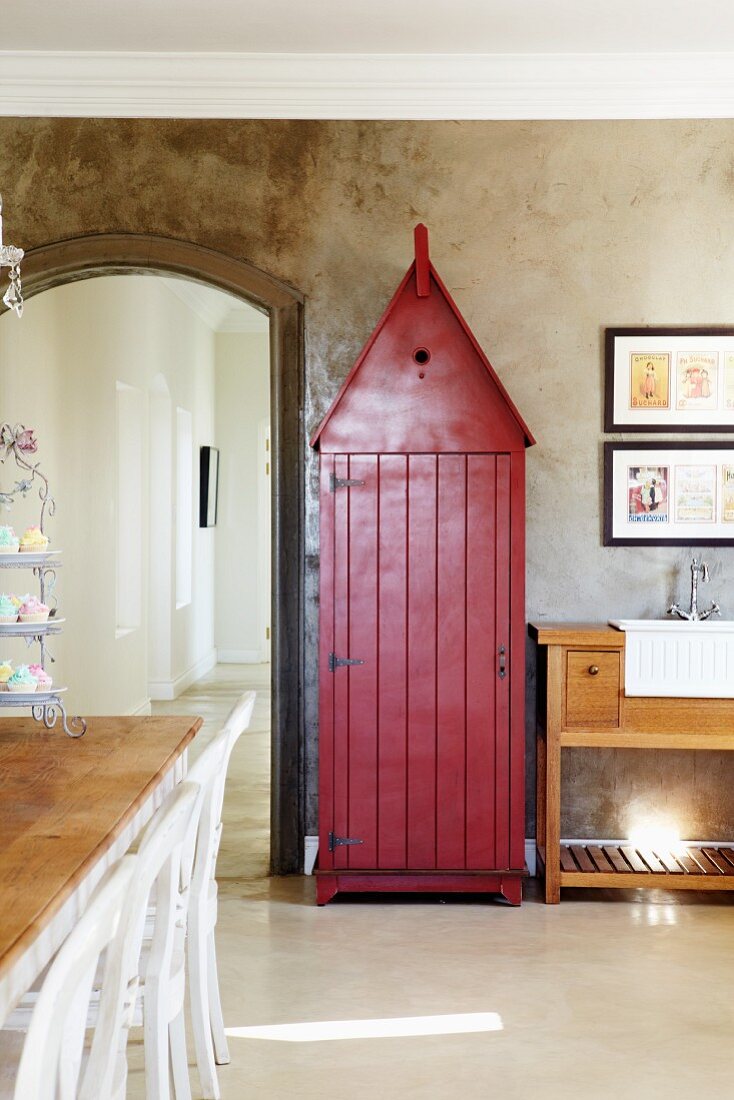 Former sentry box painted rust red in dining room against concrete-effect wall and next to arched doorway