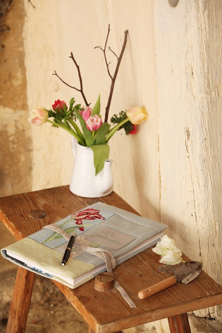 Selbstgemachter Stoffeinband mit Stickerei und Blumenstrauss auf rustikalem Holztischchen