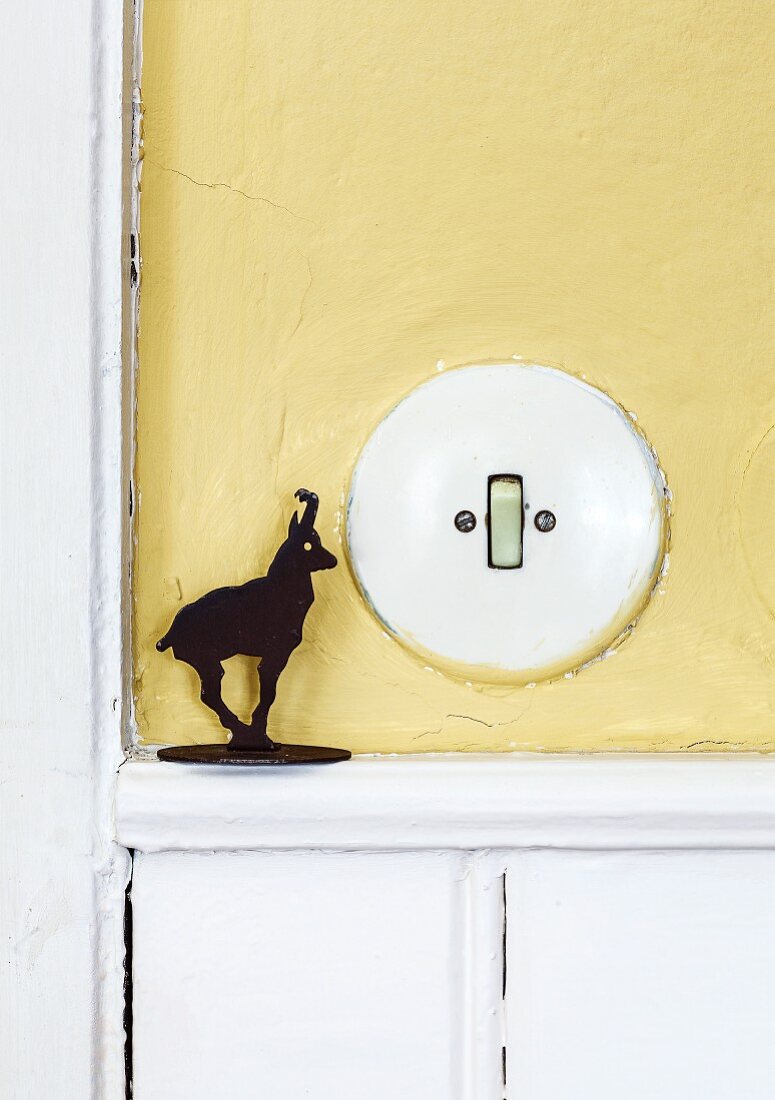 Old Bakelite light switch on wall painted pale yellow and small ibex figurine on dado rail