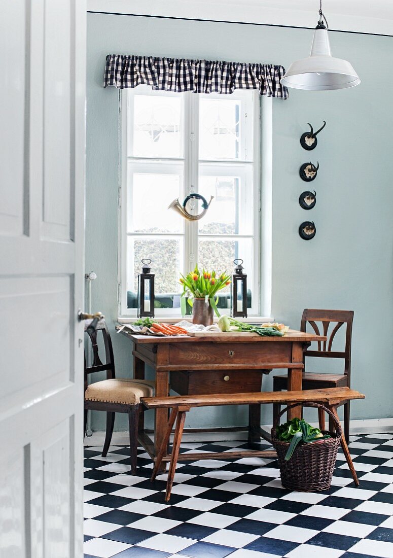 Antiker Tisch mit Stühlen im Biedermeierstil vor Küchenfenster mit altem Jagdhorn; karierte Schabracke und Fliesen im Schwarzweiss-Look