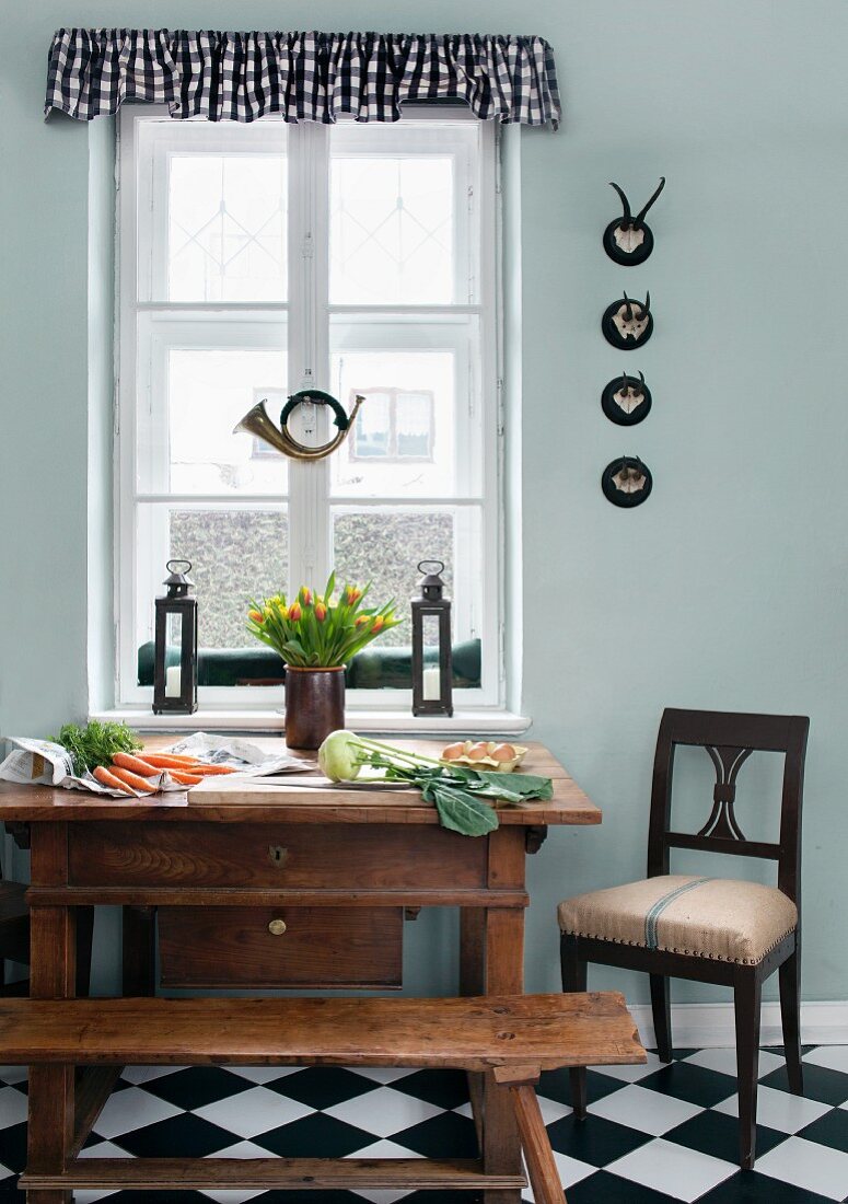 Gemüse auf Biedermeiertisch, altes Jagdhorn und Sammlung kleiner Jagdtrophäen in der Wohnküche; Sitzfläche des Stuhls mit altem Mehlsack bezogen