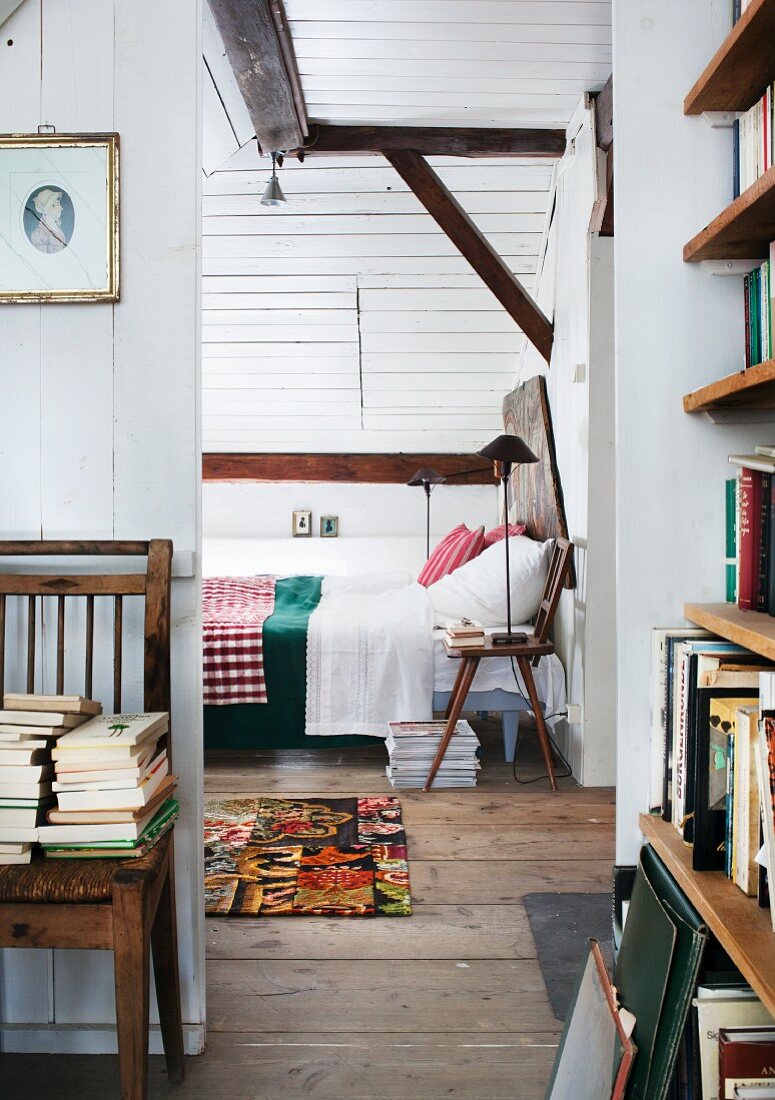 Attic guest room with white clapboard walls, many books and board chair used as bedside table