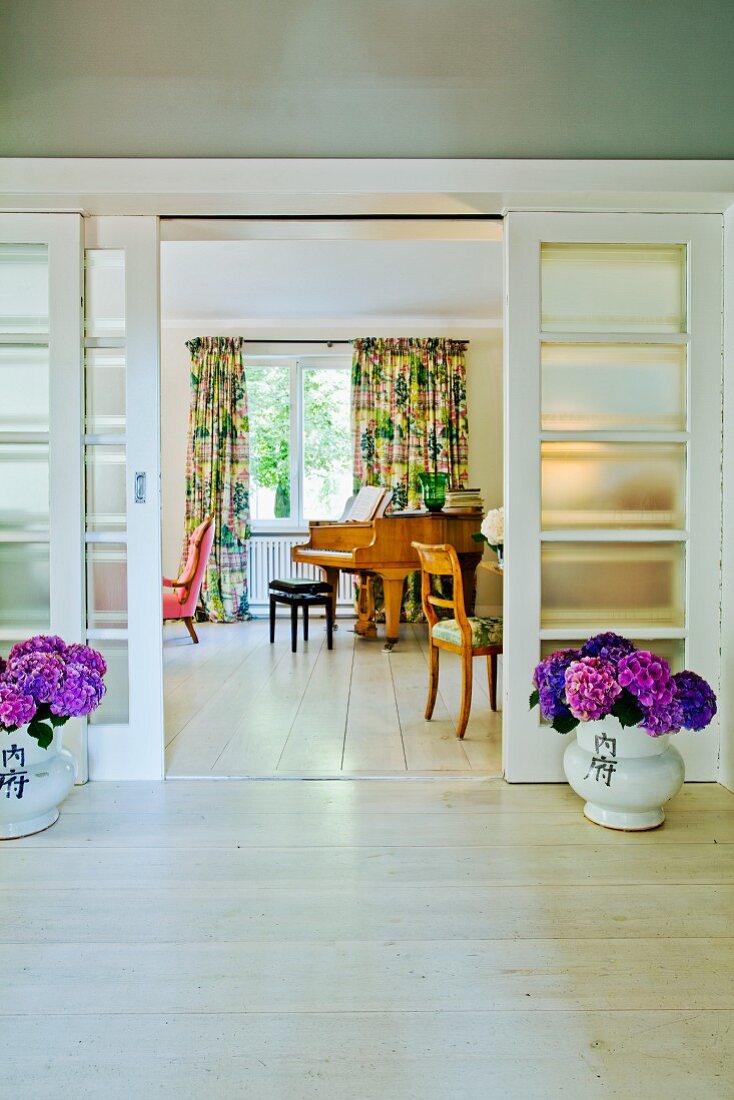 Blick in Wohnraum mit Glasschiebetüren aus den 30er Jahren, flankiert von violetten Hortensien auf hellen Holzdielen